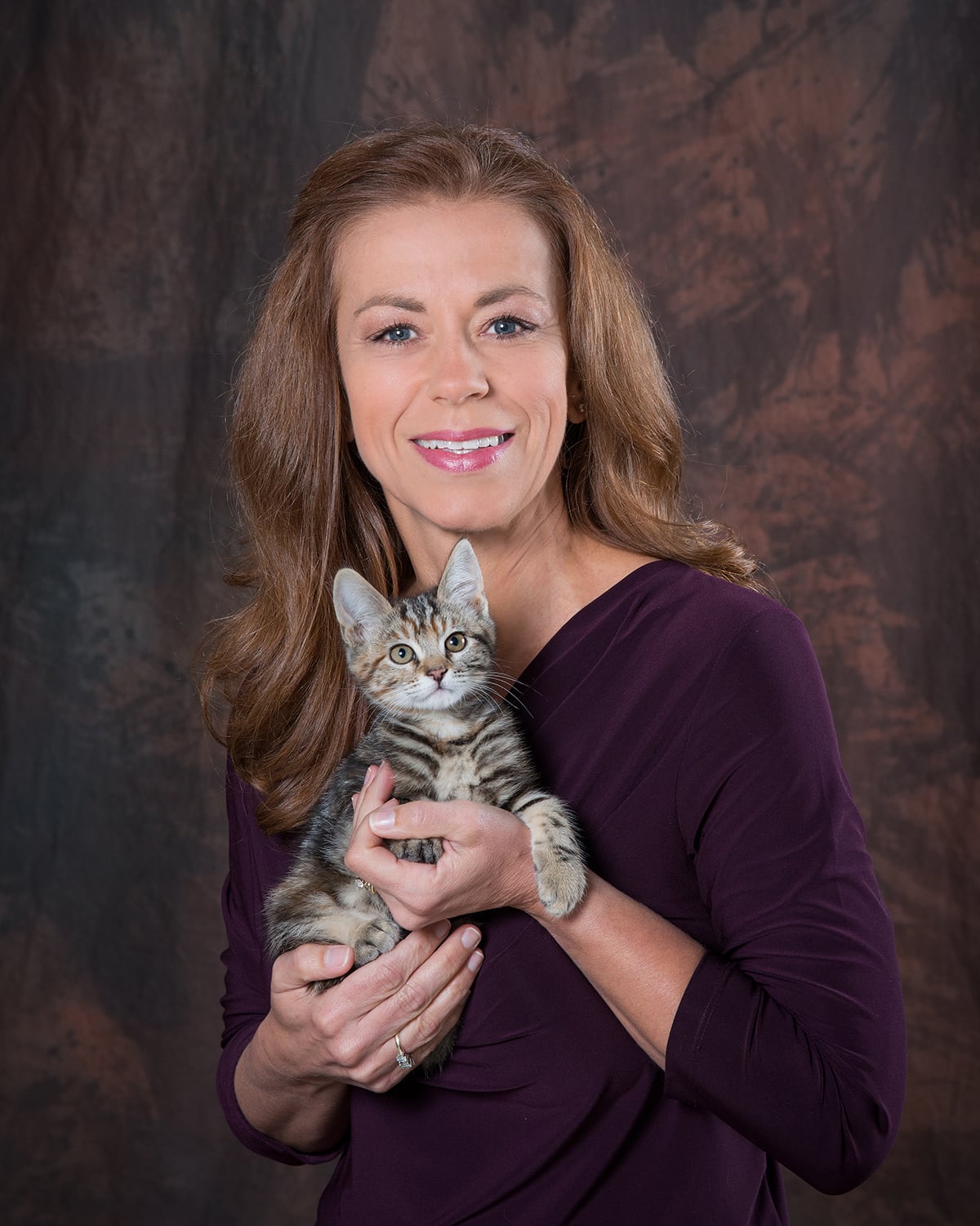 Kristi Brooks smiling in a purple blouse. She is holding a tabby kitten.
