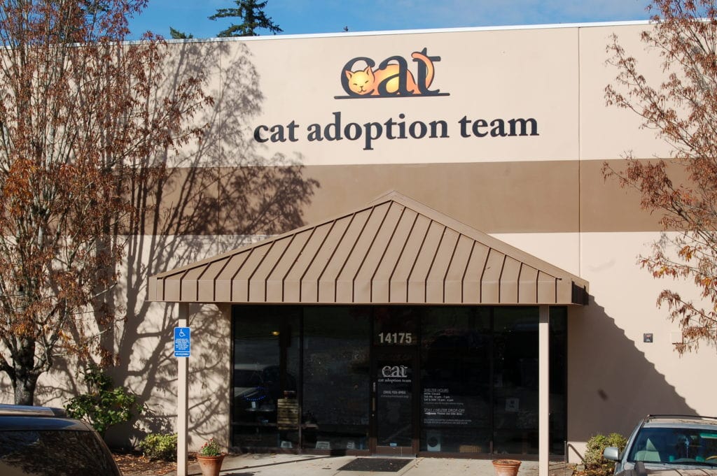 The entrance to Cat Adoption Team is flanked by two trees and the organization's logo is featured prominently on the building above the front porch.