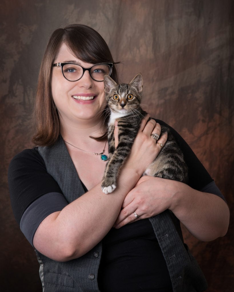 Headshot of Bobbie Winchell. She wears glasses and is holding a tabby kitten near her face.