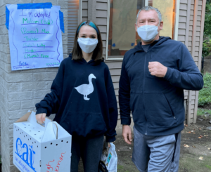 Two adopters stand outside a CAT foster home holding a cardboard cat carrier.