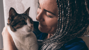 Close up a person with dark braided hair holding a tabby-and-white colored cat almost nose to nose