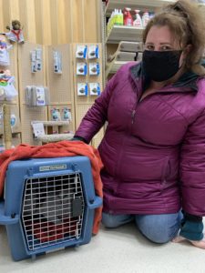 A woman kneels next to a cat carrier