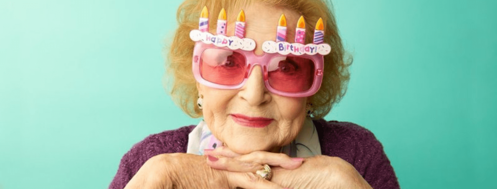 Close up image of Betty White's face. Betty is wearing fun glasses with Happy Birthday and Candle decorations on them.