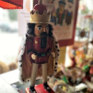 A nutcracker with dark hair and beard and dressed like a king stands on a counter while a poster showing gnomes hangs in the background.