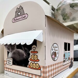 A cardboard box fashioned to look like a small coffee shop with an order window. Pusheen branding and small pastry decorations can be seen,