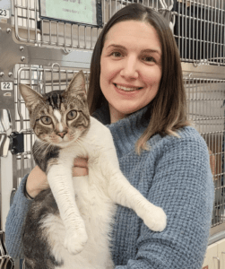 Brittany stands holding a tabby and white cat in front of a bank of kennels.