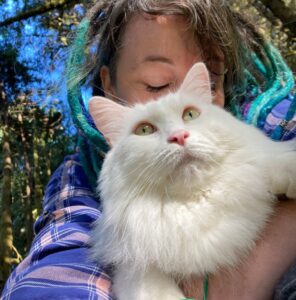 A close-up of Rumi, a fluffy white cat, being hugged from behind by his person Melanie.