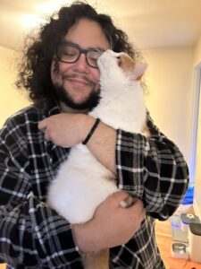 A person with curly dark hair wearing a blue-and-black shirt holds a white-and-orange cat. It seems like a blissful encounter