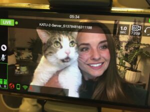 A person holds a white-and-brown cat up to their face. They both appear on a replay of a video screen.